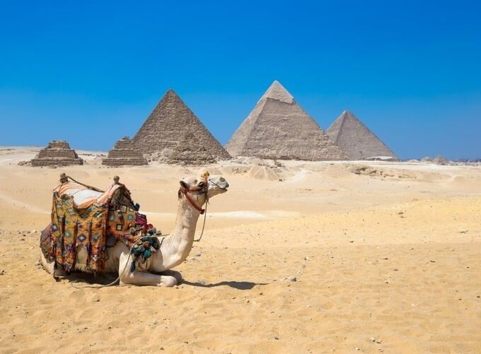 Camel riders posing near the iconic Pyramids of Giza under sunlight